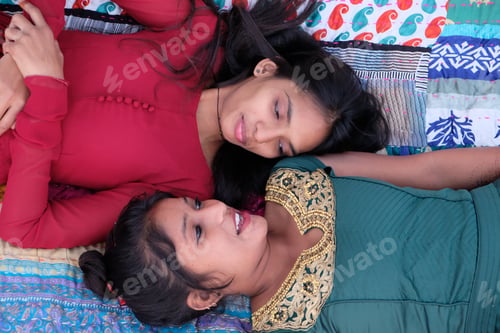 Preview: Two Young Indian Female Friends Lying On Colorful Fabrics And Talking To Each Other