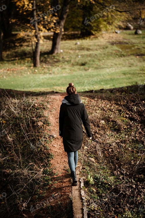 Preview: A Rear View Of A Woman Wearing A Black Hoddie Coat Walking On A Path Through The Meadow