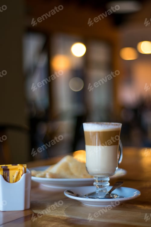 Preview: A Vertical Shot Of A Cup Of Caffe Macchiato Next To Pastries And Sugar Packets On A Wooden Surface