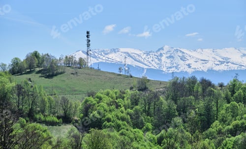 Preview: A Landscape Of Greenery Surrounded By Rocky Mountains Covered In The Snow Under The Sunlight