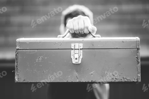 Preview: A Greyscale Shot Of A Male Holding A Toolbox In Front Of His Face