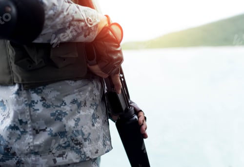 Preview: Selected Focus Navy Hand Holding Rifle Standing On Guard In Sunlight With Ocean In Background