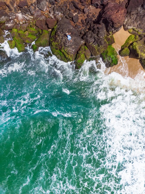 Preview: A Vertical Aerial Shot Of A Female With Blue Dress Lying On The Rocky Beach