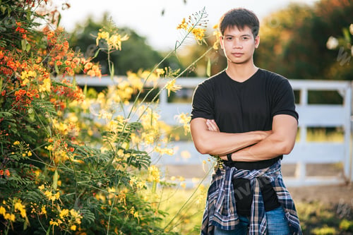 Preview: The Male Traveler Wears A Black Shirt And Stands In A Flower Garden.