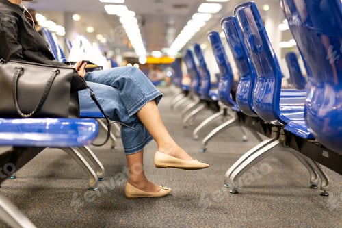 Preview: Selected Focus Woman Sitting Cross Legged With Cream Color Shoes Holding Cell Phone In Airport