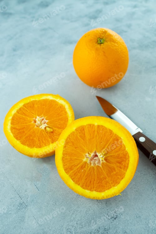 Preview: A Vertical Closeup Shot Of Fresh Ripe Oranges And A Sharp Knife On A Light Blue Background