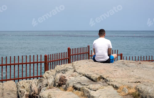 Preview: Man Sitting On The Rock Doing Meditation By The Sea In Day Time