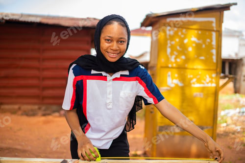Preview: A Professional Female African Carpenter Smiling As She Takes A Measurement Of Wood