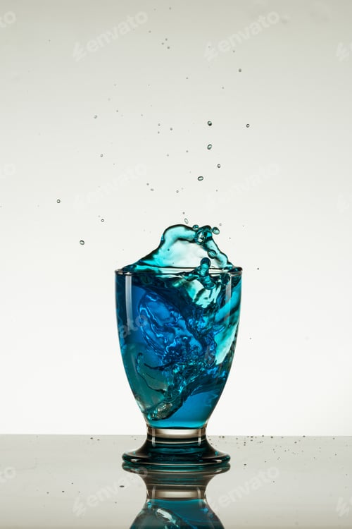 Preview: A Vertical Shot Of A Glass Of Blue, Splashing Drink Isolated On A Reflective Surface