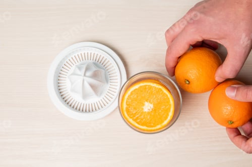 Preview: A Top View Of A Person Holding Fresh Oranges Next To A Juicer