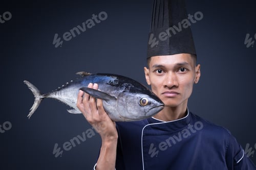 Preview: A Portrait Of An Asian Executive Chef In His Blue Uniform, Black Apron And Black Hat On Grey
