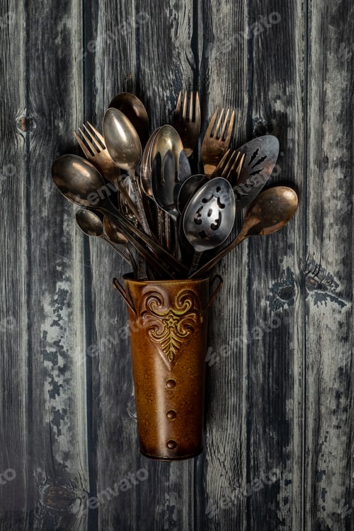 Preview: A Top Down View Of A Bronze Metal Vase Filled With Antique Cutlery And Utensils.