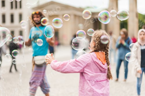 Preview: Children Playing With Colorful Soap Bubbles Floating In The Foreground. Street Performer, Busker
