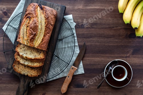 Preview: A Top Down View Of A Sliced Banana Loaf On A Wooden Board With A Cup Of Coffee Against A Dark