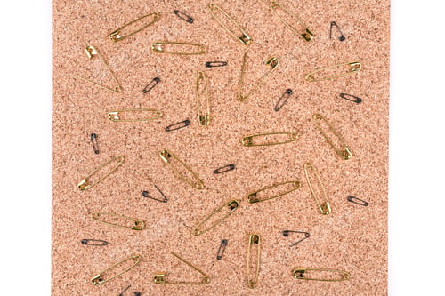 Preview: Gold Safety Pins Spread Out On A Piece Of Cork Board