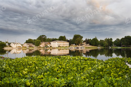 Preview: Boats Sit Docked At The Side Of A Lake With Water Lilies In The Foreground.