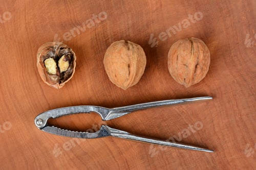 Preview: High Angle Shot Of Three Walnuts And A Nutcracker On A Wood Surface, One Nut Is Cracked In Half
