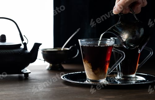 Preview: A Close Up Of Cream Being Poured Into Steaming Hot Tea Against A Dark Background With Light Coming