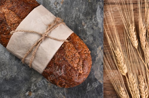 Preview: Top View Of A Loaf Of Multi-Grain Bread On A Slate Surface And Wheat Stalks.