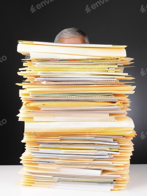 Preview: An Overworked Businessman Sitting At His Desk Hidden Behind A Large Stack Of Files. Vertical Format