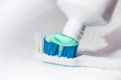 Preview: Macro Closeup Of Toothpaste A Yellow And Orange Toothbrush On A Textured White Background