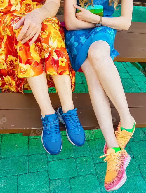 Preview: View Of Legs Of Mother And Daughter Wearing Colorful Dresses While Sitting On Wooden Bench Against