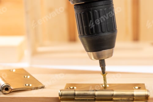 Preview: Closeup Of An Electric Drill With Screwdriver Bit And Wood Screws Fastening A Door Hinge