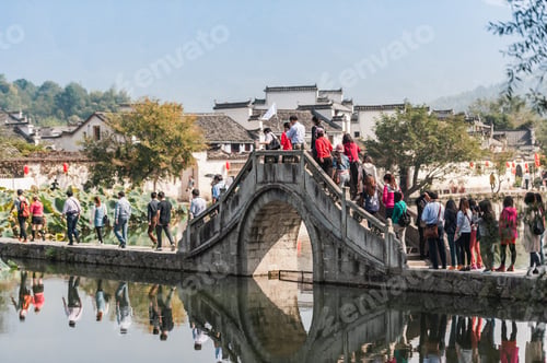 Preview: Tourists Heading Across The Bridge To Visit Hongcun Village, China. White Buildings With Ornate
