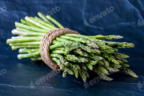 Preview: A Bunch Of Asparagus Spears Laying Down With The Tops Facing Forward Against A Dark Background.