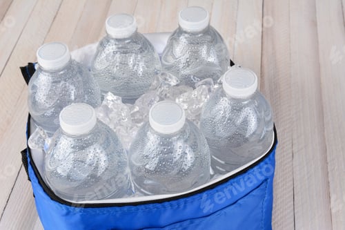 Preview: Closeup Of Six Plastic Water Bottles And Ice In A Collapsible Cooler On A White Wood Table