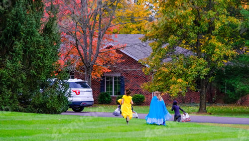 Preview: Three Kids Run Across Lawn Carrying Bags With Sweets On Halloween; Two Girls Wear Bright Dresses