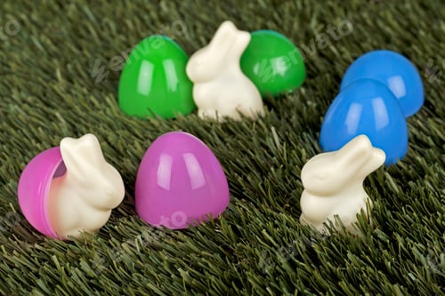 Preview: Plastic Easter Eggs With White Chocolate Easter Rabbits On Grass Background