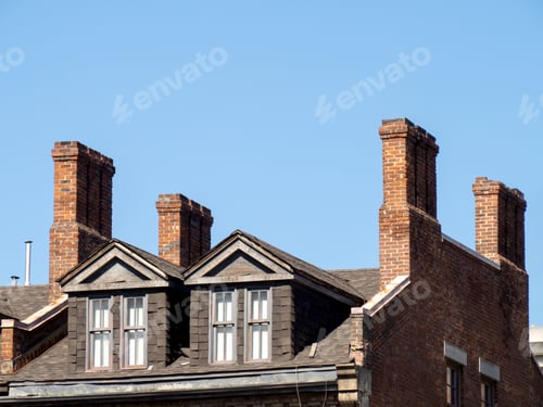 Preview: Very Old Multiple Flue Chimneys On An Old Brick Building With Dormers And Windows In The Roof