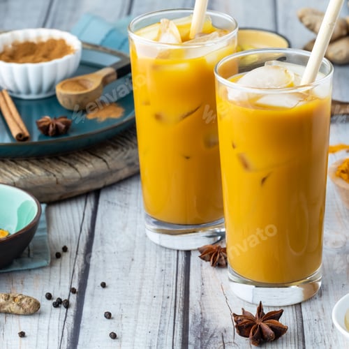 Preview: Close Up Of Two Glasses Of Ice Cold Golden Milk Surrounded By Ingredients To Make Golden Milk