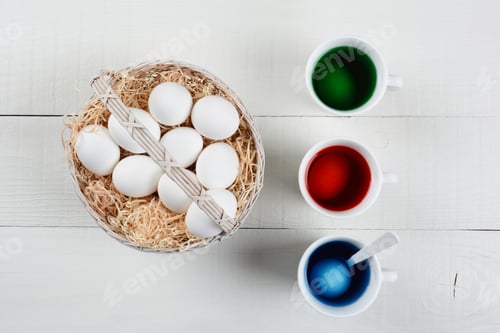 Preview: High Angle Shot Of A Basket Full Of Eggs To Be Dyed For Easter. Three Cups Of Dye With Eggs Soaking