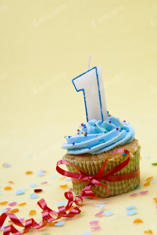Preview: Cupcake With Number One Candle And Ribbon Against Yellow Background.