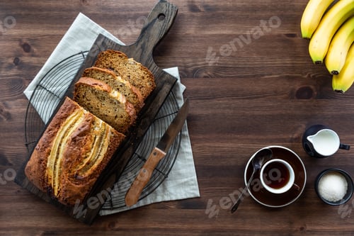 Preview: A Top Down View Of A Sliced Banana Bread On A Wooden Board With A Cup Of Coffee And Cream And Sugar.