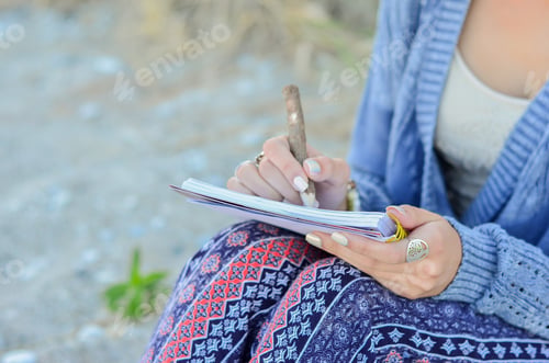 Preview: Young Woman Sitting In Sand On Beach Writing In Journal