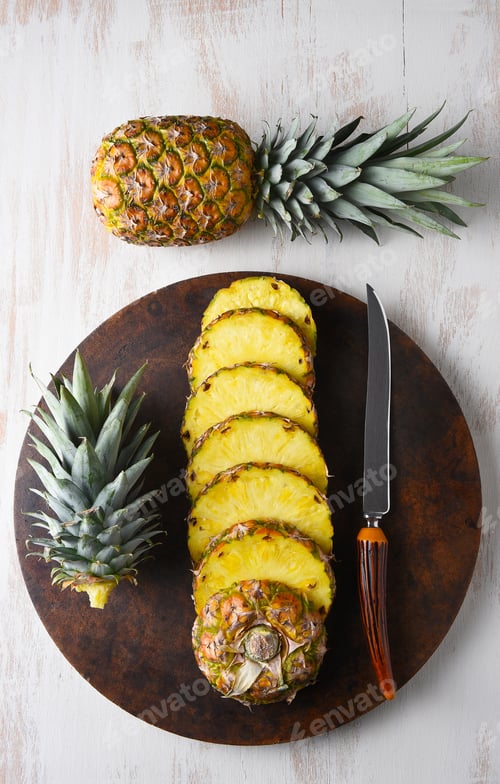 Preview: High Angle View Of A One Cut Pineapple And A Pineapple. On A Round Stone Cutting Surface, With