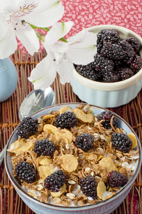 Preview: High Angle Shot Of Bowl Of Blackberry Fruits And Cereal With Flower Vase On Mat.
