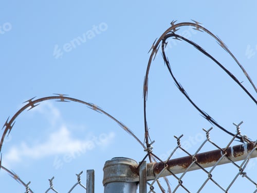 Preview: Razor Wire Coiled On Top Of A Chain Link Fence Isolated On A Blue Sky