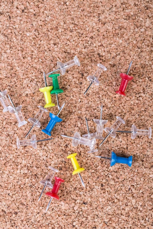 Preview: Scattered Pile Of Multicolored Thumb Tacks On A Brown Cork Board
