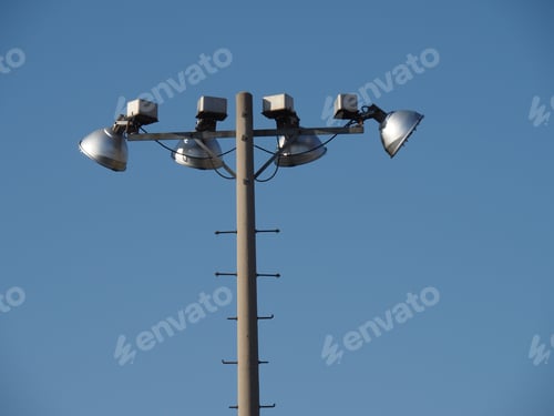 Preview: Four Mercury Vapor Stadium Lights At The Top Of A Concrete Pole Against A Blue Sky
