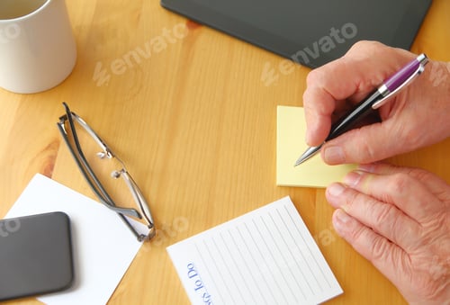 Preview: A Man Holds A Pen Over A Desk With Tablet, Phone, Notepads, Glasses, Coffee Cup And Copy Space