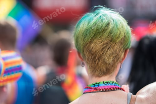 Preview: Young Woman With Green Hair In A Crowd Celebrating Pride Parade. Wearing Bright Rainbow Ribbons