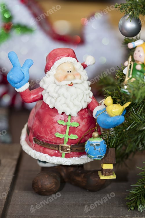 Preview: Brightly Colored Santa Claus Ornament Holding Presents Next To A Christmas Tree