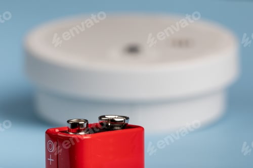 Preview: A Red Nine Volt Battery With A Home Fire Detector In The Background