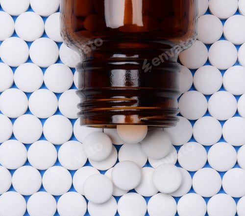 Preview: Round White Pills In Rows With A Brown Glass Prescription Bottle Laying On Top. High Angle View.