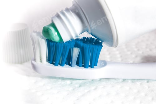 Preview: Closeup Of A Toothpaste Starting To Be Squeezed Onto A Blue And Turquoise Toothbrush On A Textured