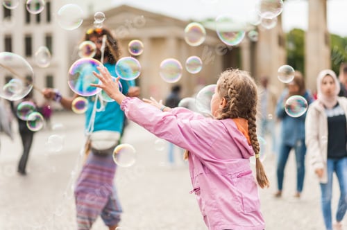 Preview: Children Playing With Colorful Soap Bubbles Floating In The Foreground. Street Performer, Busker